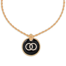Load image into Gallery viewer, Close-up of a round black epoxy pendant with clear rhinestone interlocking rings and gold-tone trim.