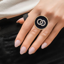Load image into Gallery viewer, Model wearing a round black epoxy statement ring with interlocking rhinestone circles and gold-tone trim