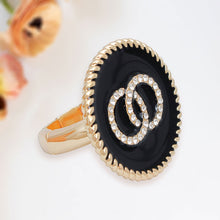 Load image into Gallery viewer, Angled view of a black epoxy statement ring with interlocking rhinestone circles, gold-tone trim, and band.