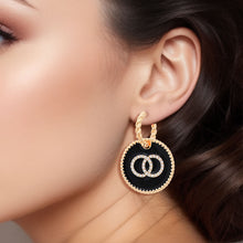 Load image into Gallery viewer, Model wearing a gold-tone twisted hoop earring with a black epoxy charm and clear rhinestone interlocking rings
